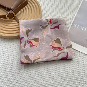 Close-up of a floral silk square scarf in lilac and pink on a textured background