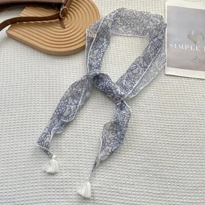 Dettaglio di un foulard in seta a fiori blu con nappe bianche su un vassoio