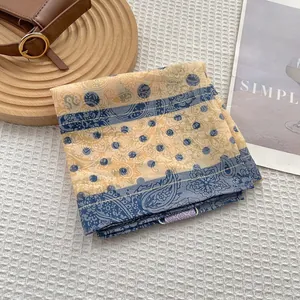 Close-up of yellow paisley and navy polka dot square scarf on white textured background