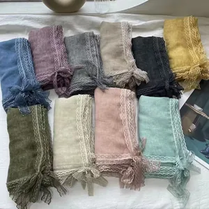 Flat lay of linen scarves with lace trim in ten assorted colors on a soft white background