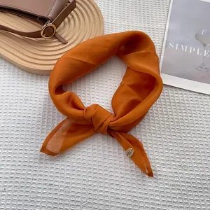 Close-up of bright orange silk scarf tied in a bow with metallic logo on waffle background
