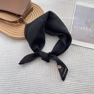 Detail view of a black silk scarf with a gold oval pendant on a white waffle texture cloth