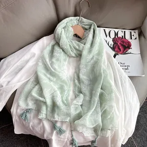 Light green cotton linen scarf with white floral print and fringe on a wooden hanger