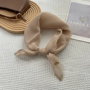 Detail of champagne silk scarf with golden logo tag on white waffle texture fabric