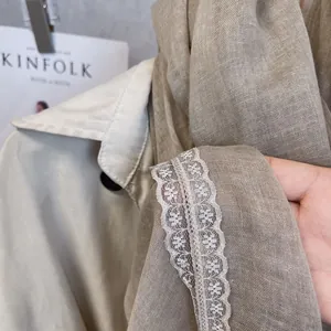 Close-up of linen blend scarf with white floral lace trim on a beige trench coat