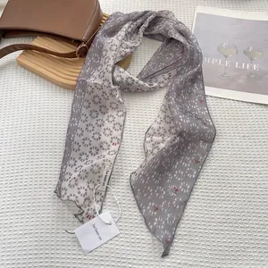 Detail of grey geometric pattern long silk scarf with premium hemmed edges on a tray