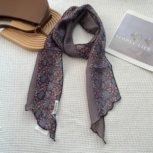 Detail of striped floral skinny silk scarf with brand tag on elegant lifestyle setup
