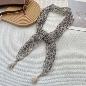 Dettaglio di sciarpa in seta leopardata con nappe su uno sfondo materico minimalista
