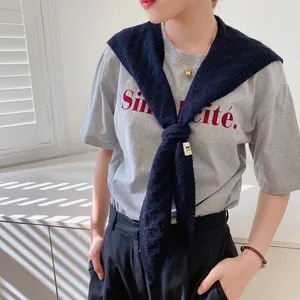 Detail of navy blue cable knit shawl over grey t-shirt with Simplicité text print