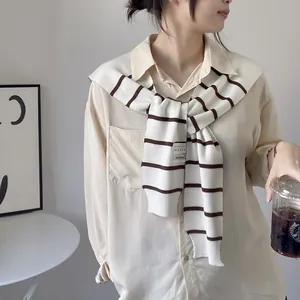 Detail of a cream long-sleeved shirt paired with a classic black and white striped shawl