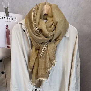 Gros plan d'une écharpe en coton et lin jaune gingembre avec pompons en dentelle blanche