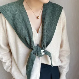 Close-up of chunky cable knit shawl in forest green paired with cream knit cardigan