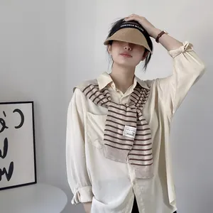 Detailed view of women's striped knit shawl draped over a classic beige button-up shirt