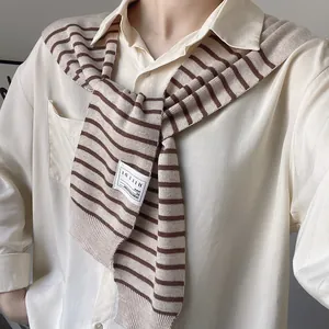 Detailed view of striped knit shawl over a cream shirt with a woven brand logo label