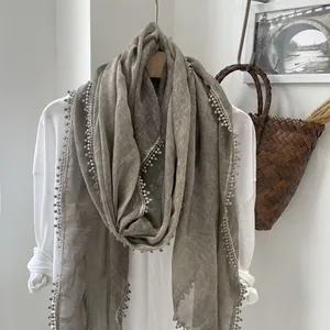 Détail d'une écharpe en lin avec bordures en dentelle et pompons sur cintre en bois