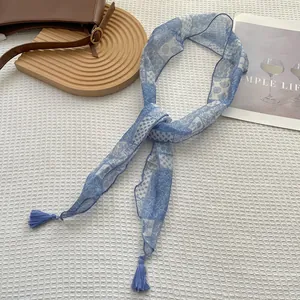Dettaglio di una sciarpa sottile azzurra a fiori con nappe su sfondo bianco strutturato