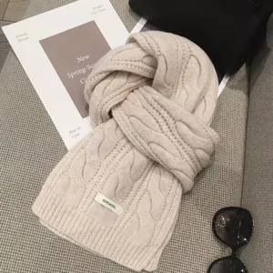 Close-up of cream white cable-knit scarf showing 100% wool material label and soft texture