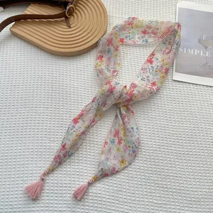 Dettaglio della sciarpa in chiffon floreale con nappe rosa su vassoio rustico