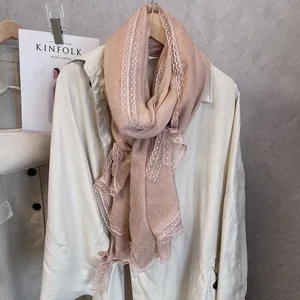 Detailed view of dust pink scarf with white lace trim layered over a beige trench coat