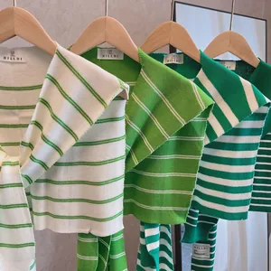 Detail view of four green and white striped knit shawls on wooden hangers for layering