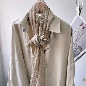 Elegant linen-colored lace scarf with white micro-polka dots on a light trench coat