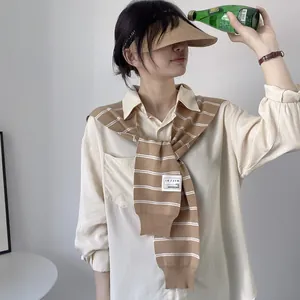 Close-up of brown striped knitted shawl styled over a beige shirt with a straw visor hat