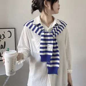 Detail of blue and white striped knit shawl with a white brand label on cotton shirt