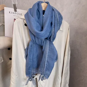 Close-up of light blue cotton linen scarf with delicate lace trim hanging on a beige coat