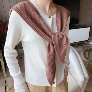 Detailed knit texture of ivory cardigan and caramel cable-knit shawl with gold-edged buttons