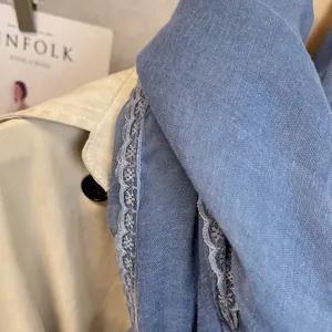 Close-up of blue cotton linen scarf with white lace trim draped on a beige trench coat