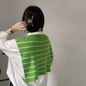 Close-up of green and white striped knit shawl layered over a white shirt with hair clip