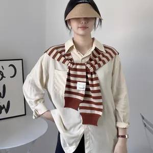 Detail of classic striped knit shawl draped over a beige shirt with a summer woven hat
