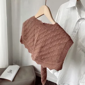 Detail of tan crochet knit shawl with diamond texture and scallop edges on a hanger