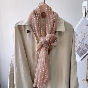 Detail of peach lace scarf with white dots and floral embroidery on a beige coat