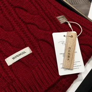 Detail of red cable knit scarf with 100% wool label and cedar wood charm