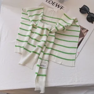 Detail of green and white striped knit shawl with brand label on a textured surface