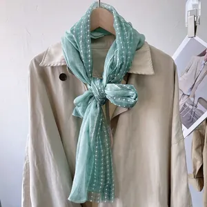 Detailed texture of mint green mesh scarf with white polka dot beads on a beige coat