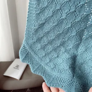 Close-up of blue knitted shawl featuring hollow diamond textures and wavy ruffle edges