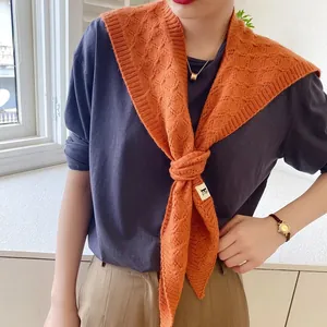 Close-up of orange knitted shawl with diamond pattern and brand label on a tied model