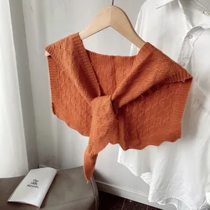 Orange knitted hollow shawl wrap with diamond patterns on a wooden hanger with white shirt