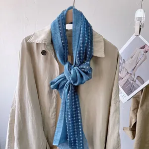 Detail of blue lace linen scarf with white polka dot lines on a beige trench coat