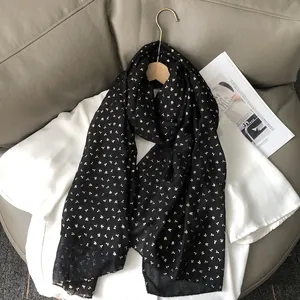 Détail de l'écharpe noire en coton et lin avec des motifs de feuilles dorées sur haut blanc