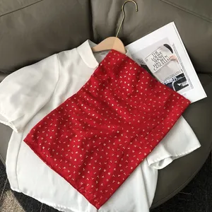 Détail de la jupe fleurie rouge avec motif cerise doré sur une chemise blanche et cintre
