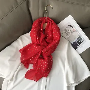 Détail de l'écharpe rouge avec imprimé trèfle doré sur un tissu léger et doux