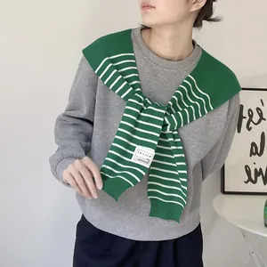 Detail of green and white striped knit shawl with brand label over a casual sweatshirt