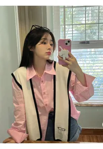 Detail view of pink long-sleeve shirt with white knit vest and black trim accent