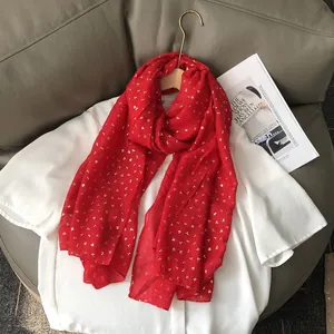 Détail d'une écharpe rouge avec motifs fleurs dorées suspendue sur un cintre en bois