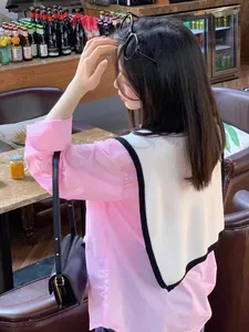 Detail view of a white knitted shawl over a pink shirt with black leather crossbody bag