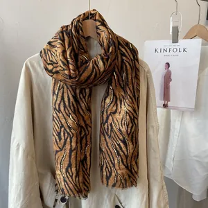 Close-up of long tiger print scarf with gold sequins on beige coat with Kinfolk book
