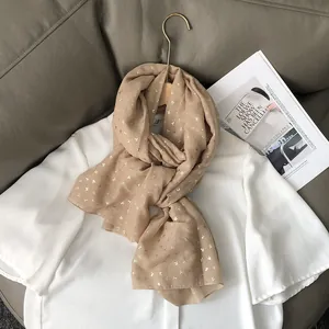 Détail d'une écharpe beige légère avec motifs de cerisiers dorés sur chemise blanche